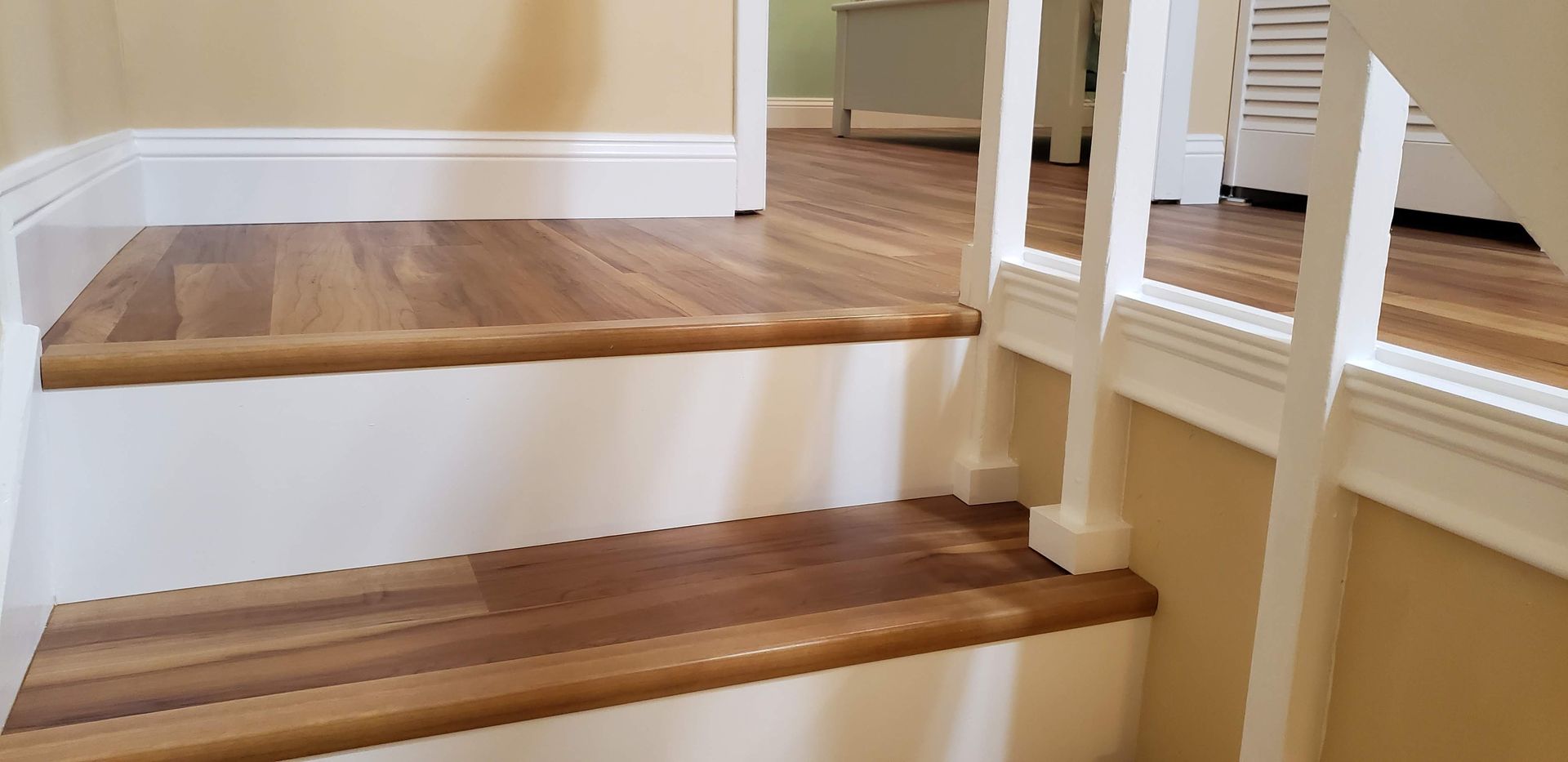 Stairs with wood grain treads, white risers, and white railings leading to a room with light-colored flooring.