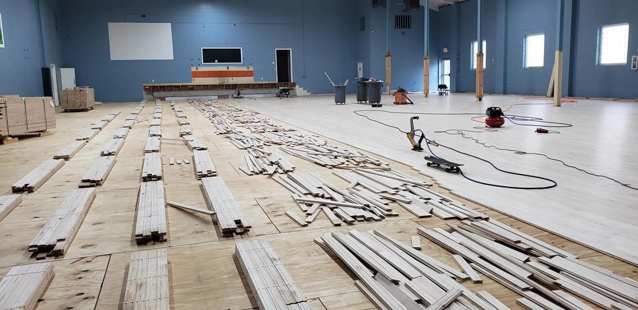 A large, blue-walled room under construction, with wood flooring being installed and piles of materials on the subfloor.