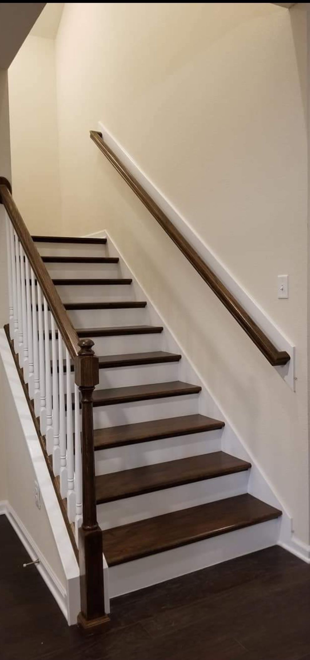 A wooden staircase with dark-stained treads and white risers, featuring a white balustrade and a dark handrail on the wall.