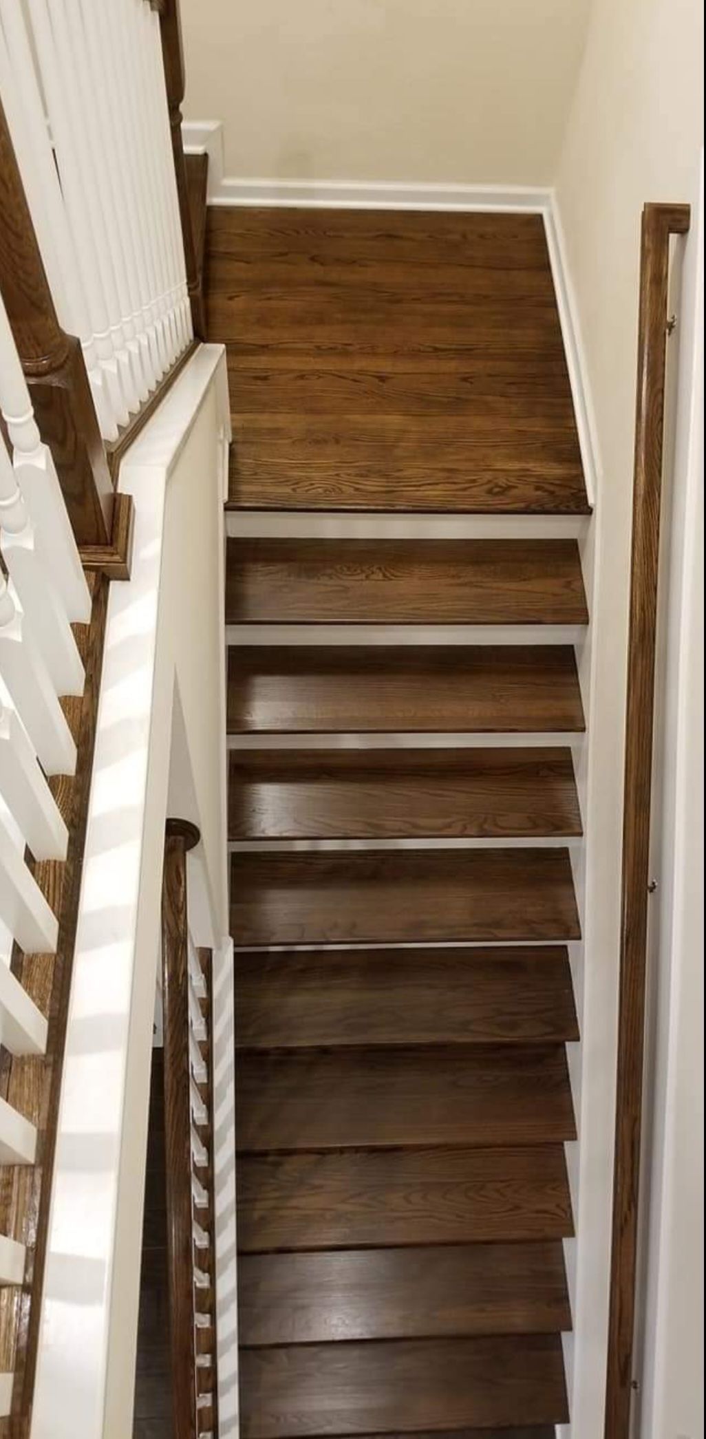Staircase looking down from the top, featuring dark wood treads, white risers, a white railing, and a rustic wood handrail.
