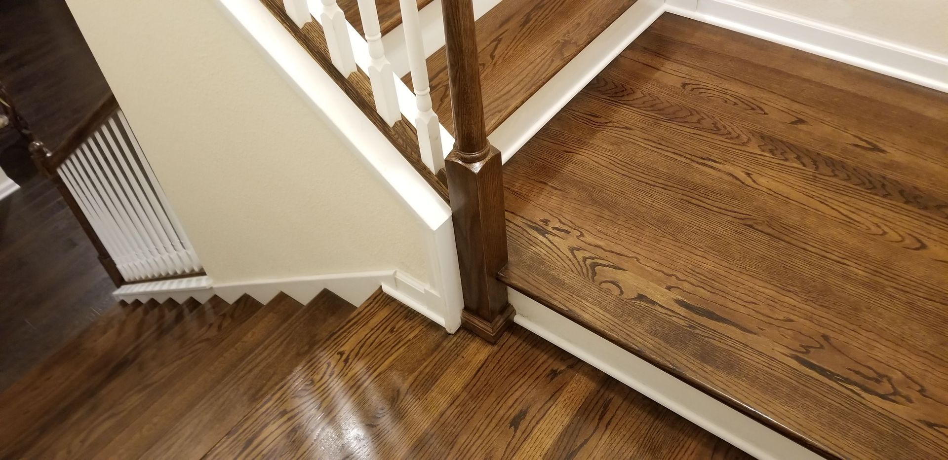 A high-angle view of hardwood stairs with white railings and risers, showing a landing and a transition to lower steps.