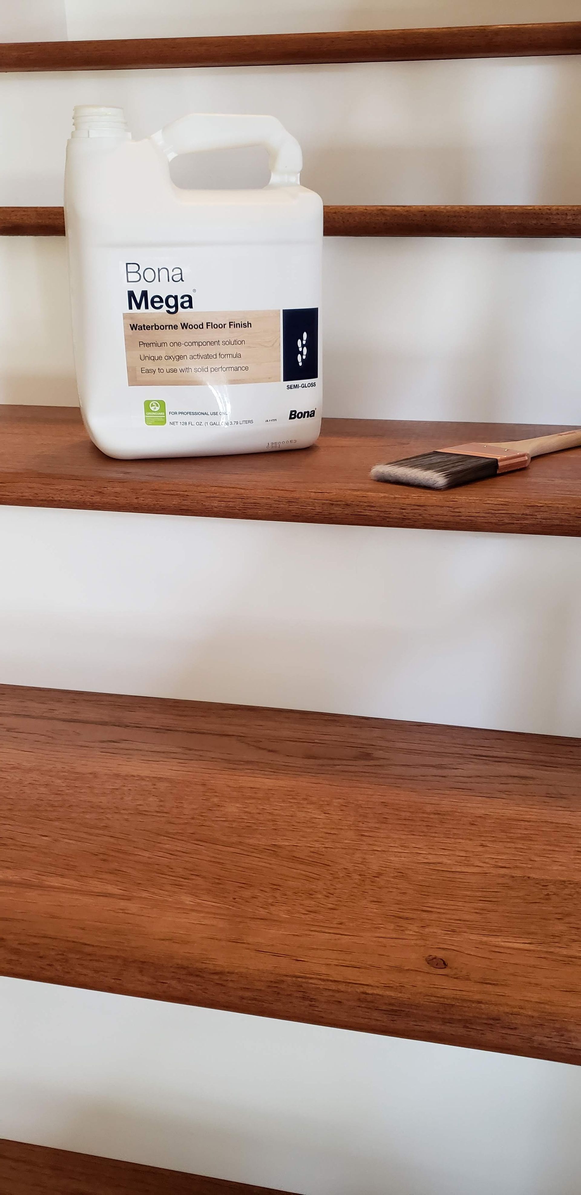 A white jug of Bona Mega floor finish and a paintbrush sitting on a wooden staircase step.