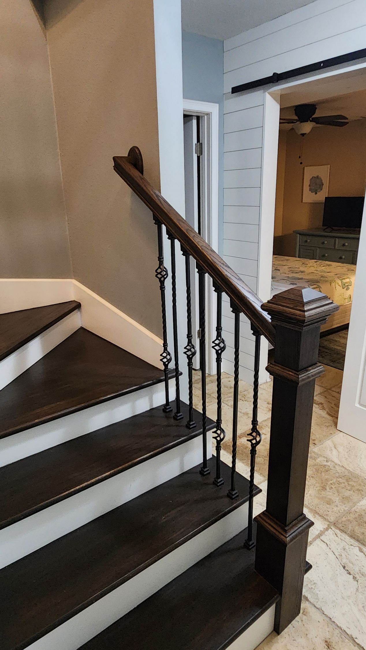 A staircase with dark wood treads and white risers, featuring a decorative iron railing and a square wood newel post.