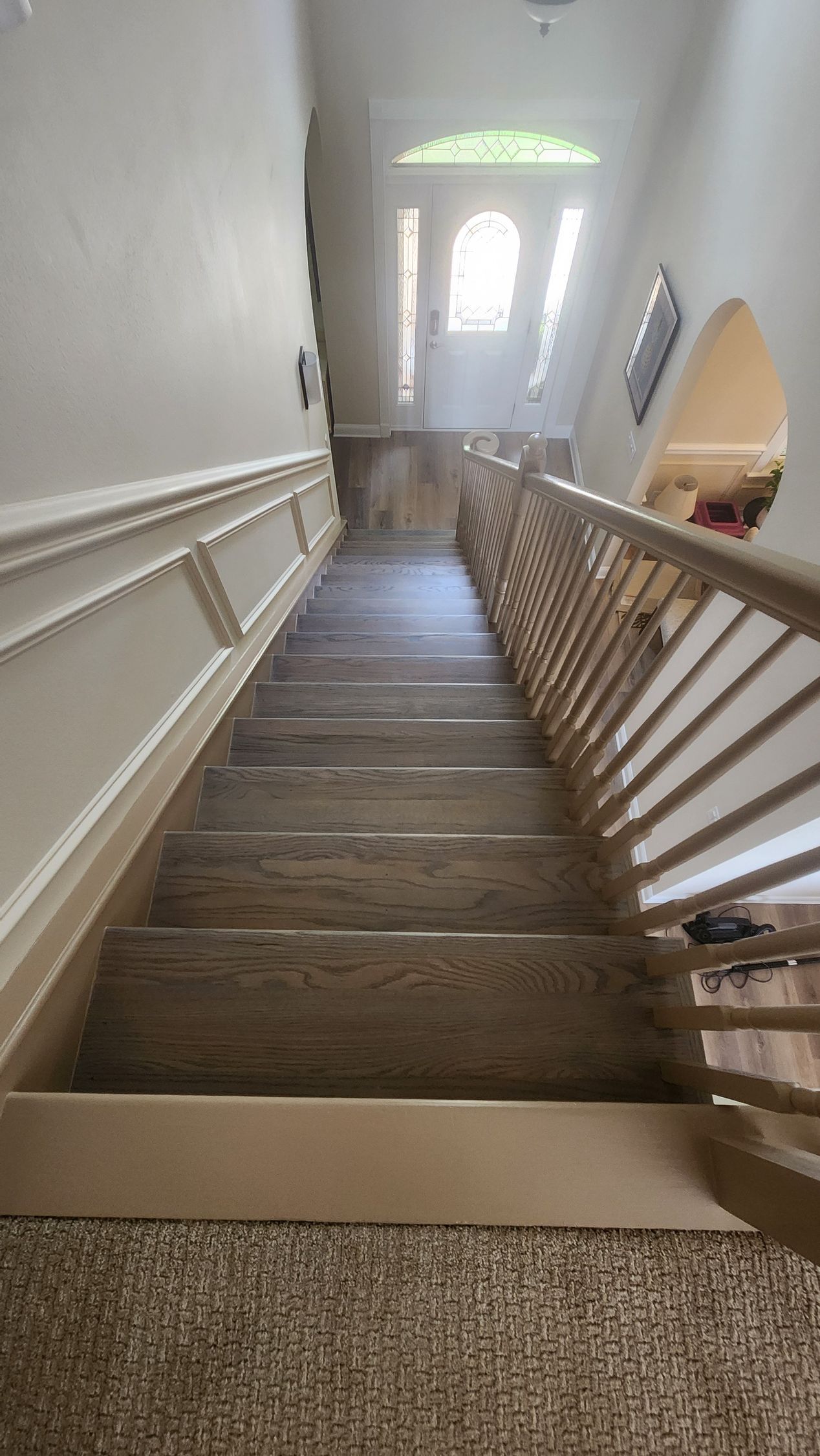 A high-angle view looking down a wooden staircase with a beige handrail and decorative molding on the adjacent white wall.