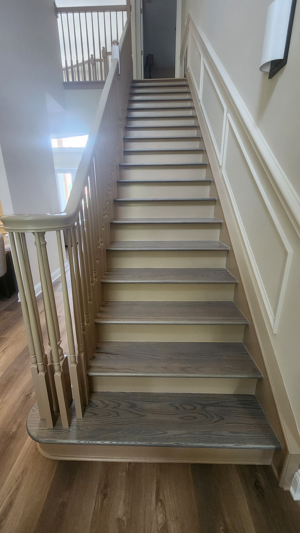 A staircase with light wood steps and a tan railing leading to an upper landing in a neutrally colored hallway.