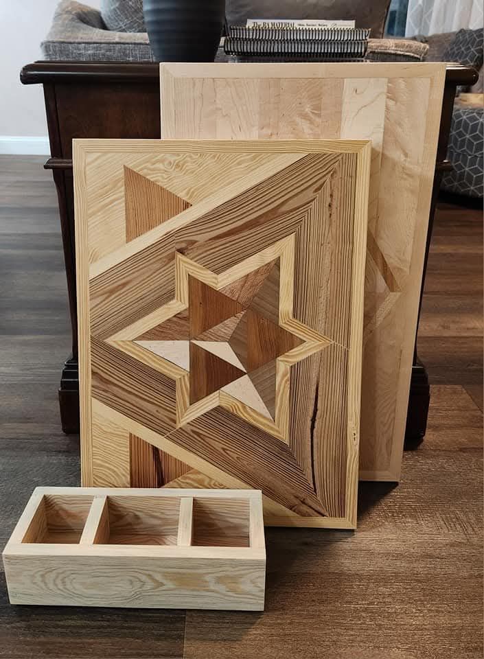 A wooden geometric star wall art piece stands in front of a plain board and beside a small three-compartment wooden tray.