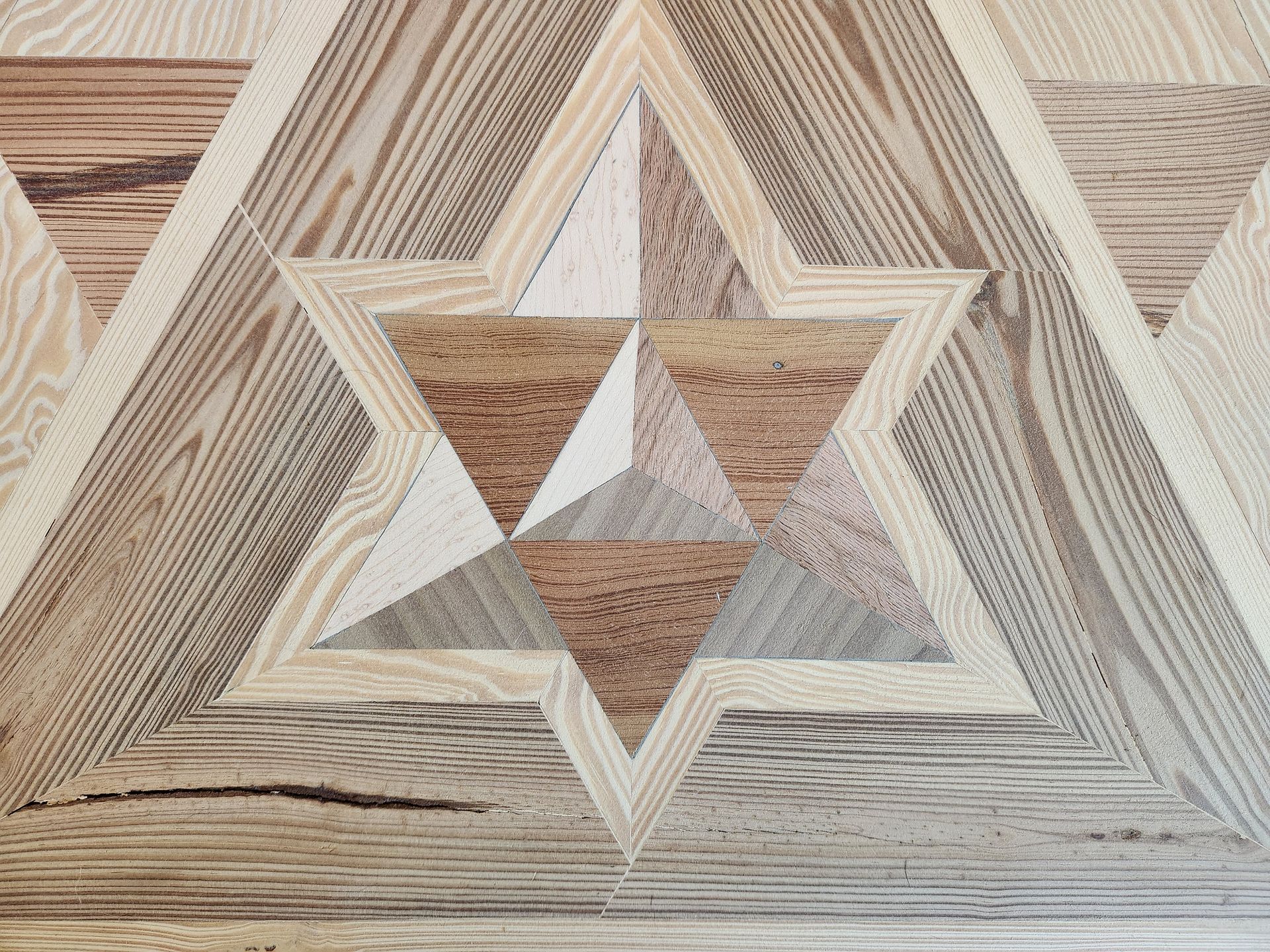 A close-up of a wooden floor featuring a six-pointed star inlay made of contrasting grain patterns and shades of brown.