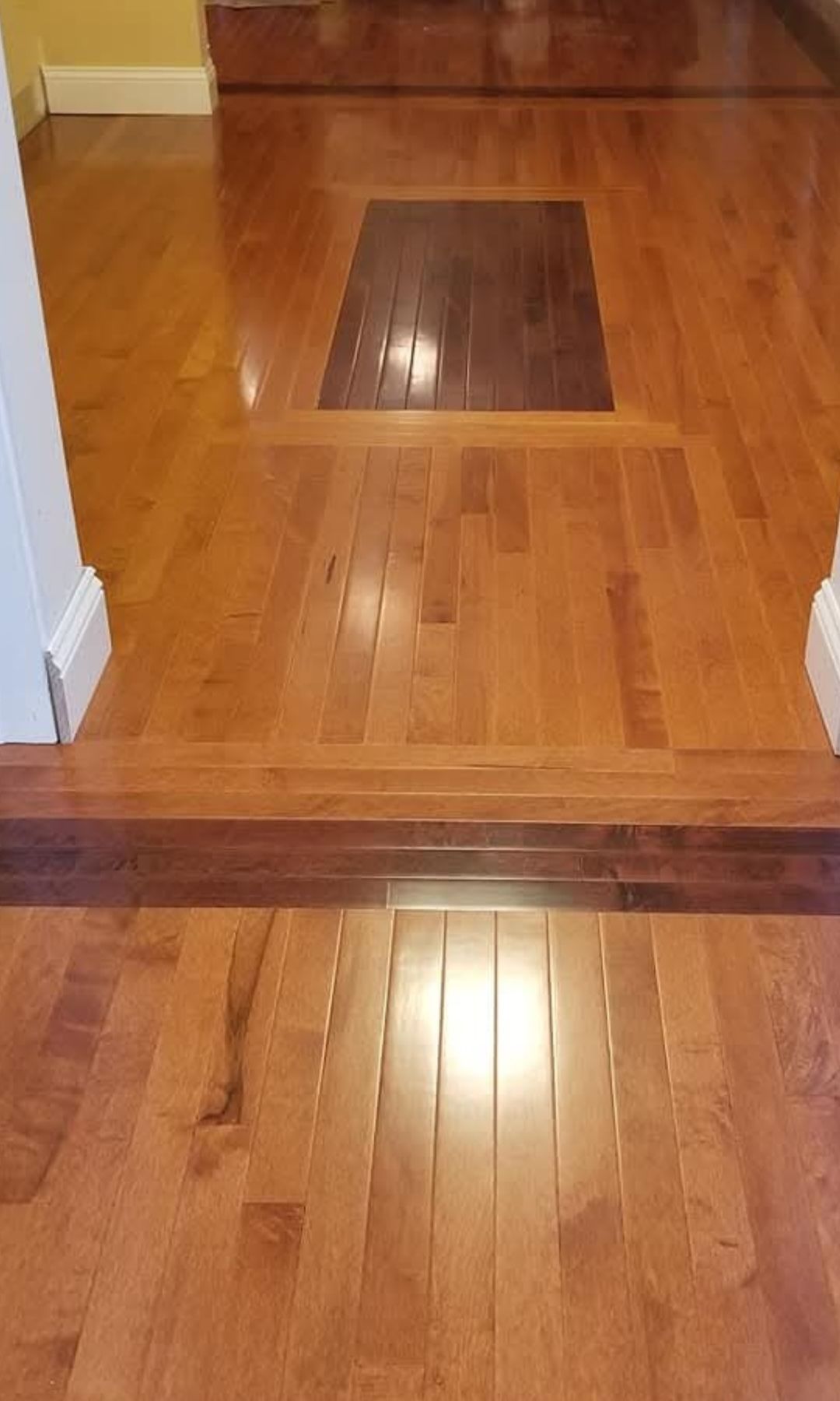 A wooden floor with a single step, featuring light brown planks and contrasting dark brown accent wood on the stair edge.