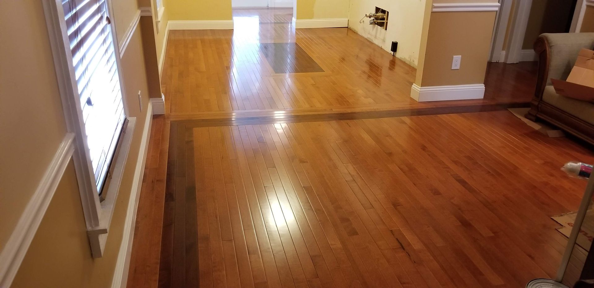 Polished hardwood floors with a dark wood border spanning between two rooms, illuminated by bright natural light.