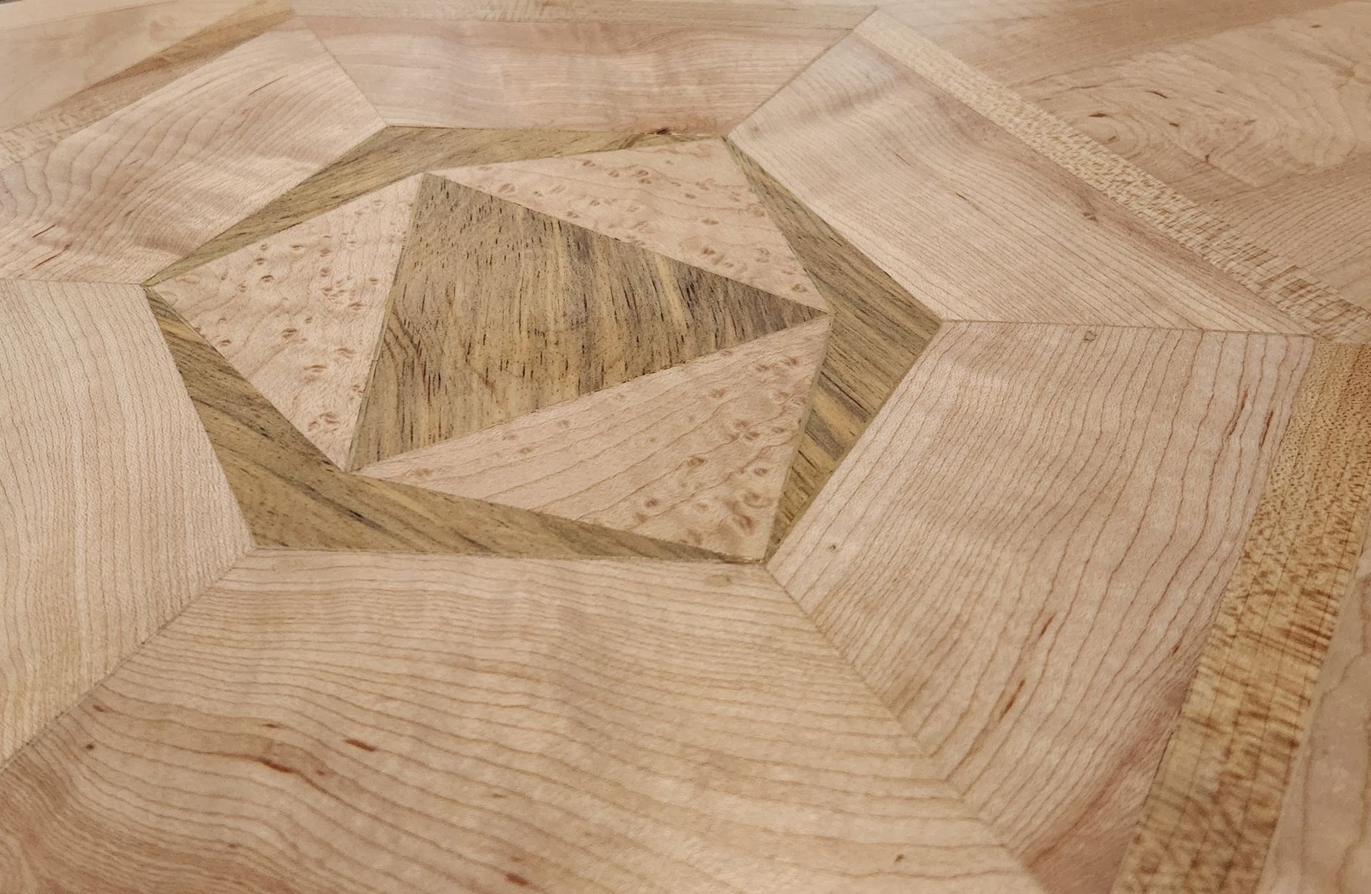 Close-up view of geometric wood flooring featuring a central pentagon pattern with alternating light and dark wood grain.