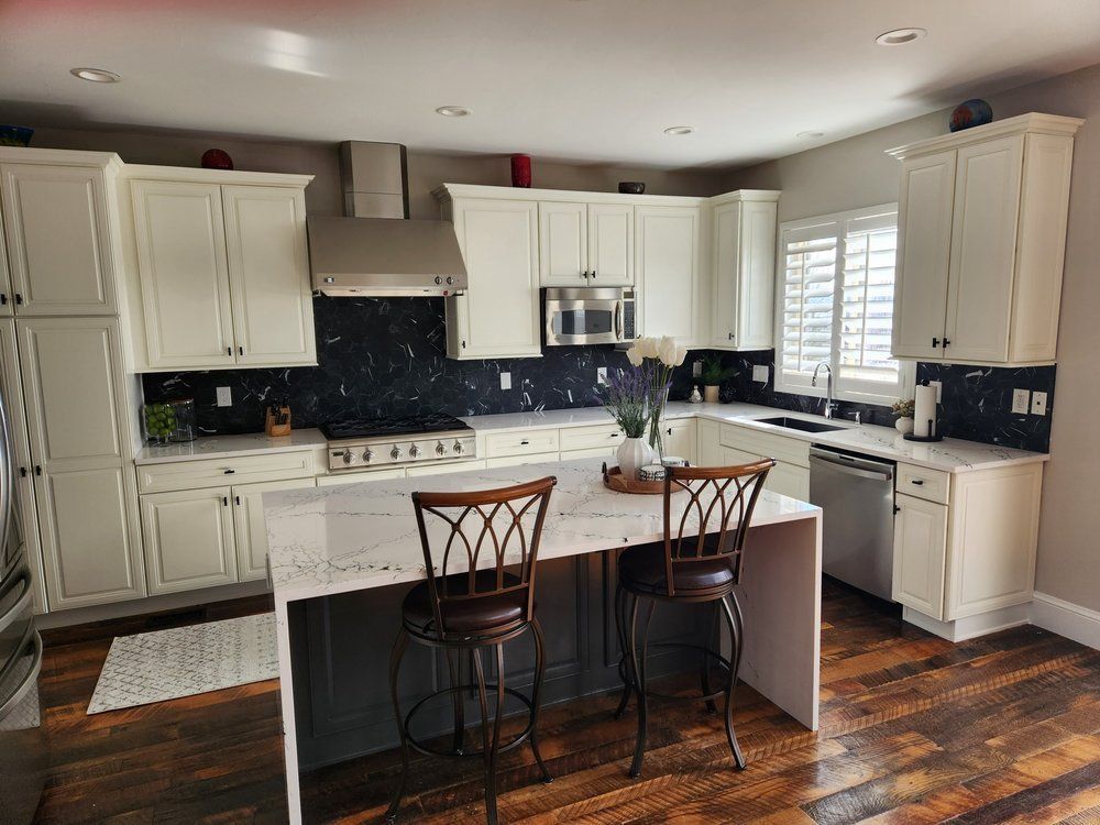 A kitchen with white cabinets , stainless steel appliances , wooden floors and a large island.
