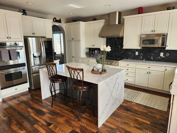 A kitchen with white cabinets , stainless steel appliances , hardwood floors and a large island.