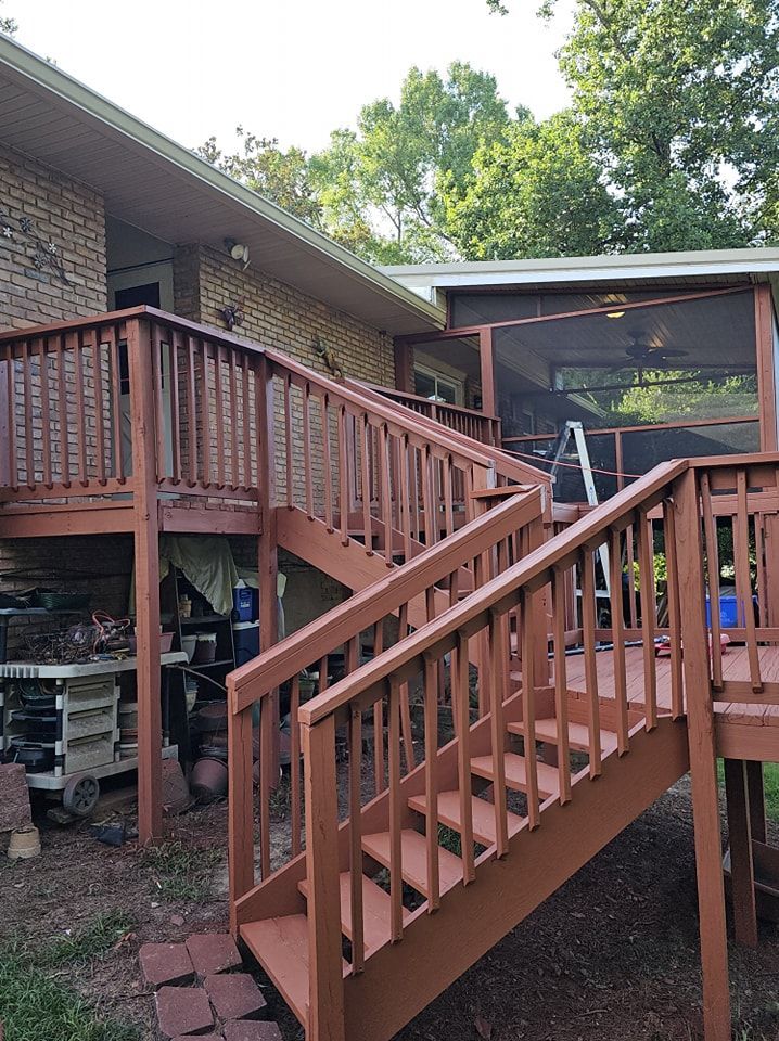 Red wooden deck and stairs next to a brick building, leading to a screened-in porch.