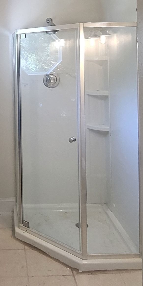 A corner shower with a clear glass door. The shower has a white base and walls.