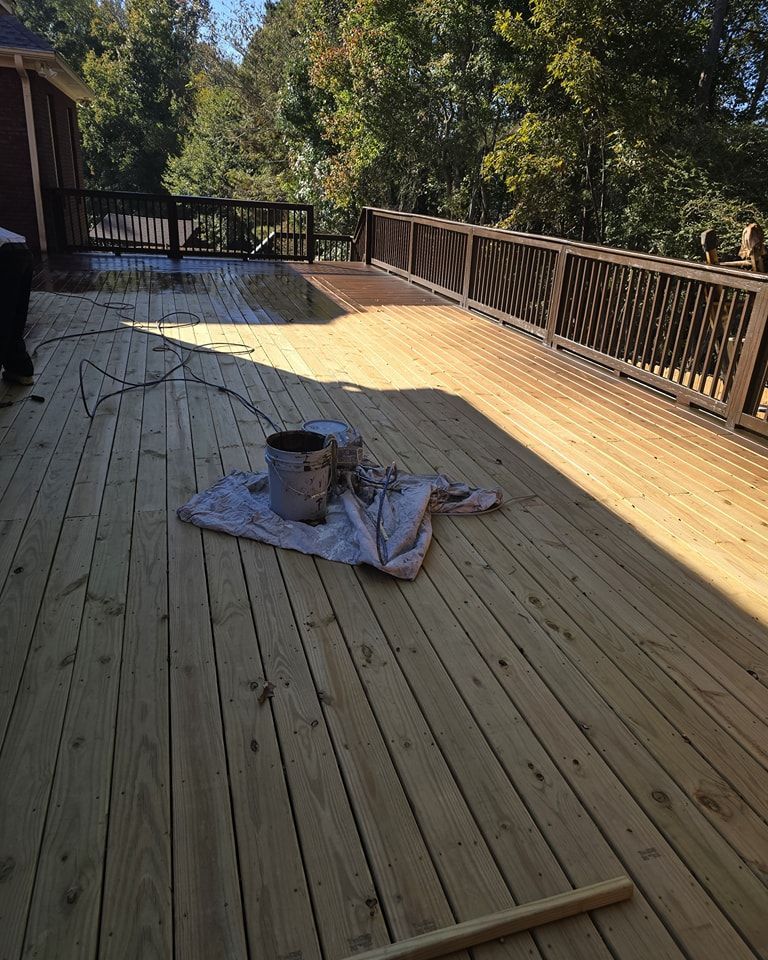 Wooden deck with railing, buckets, and a drop cloth. A sunny day with a view of trees.