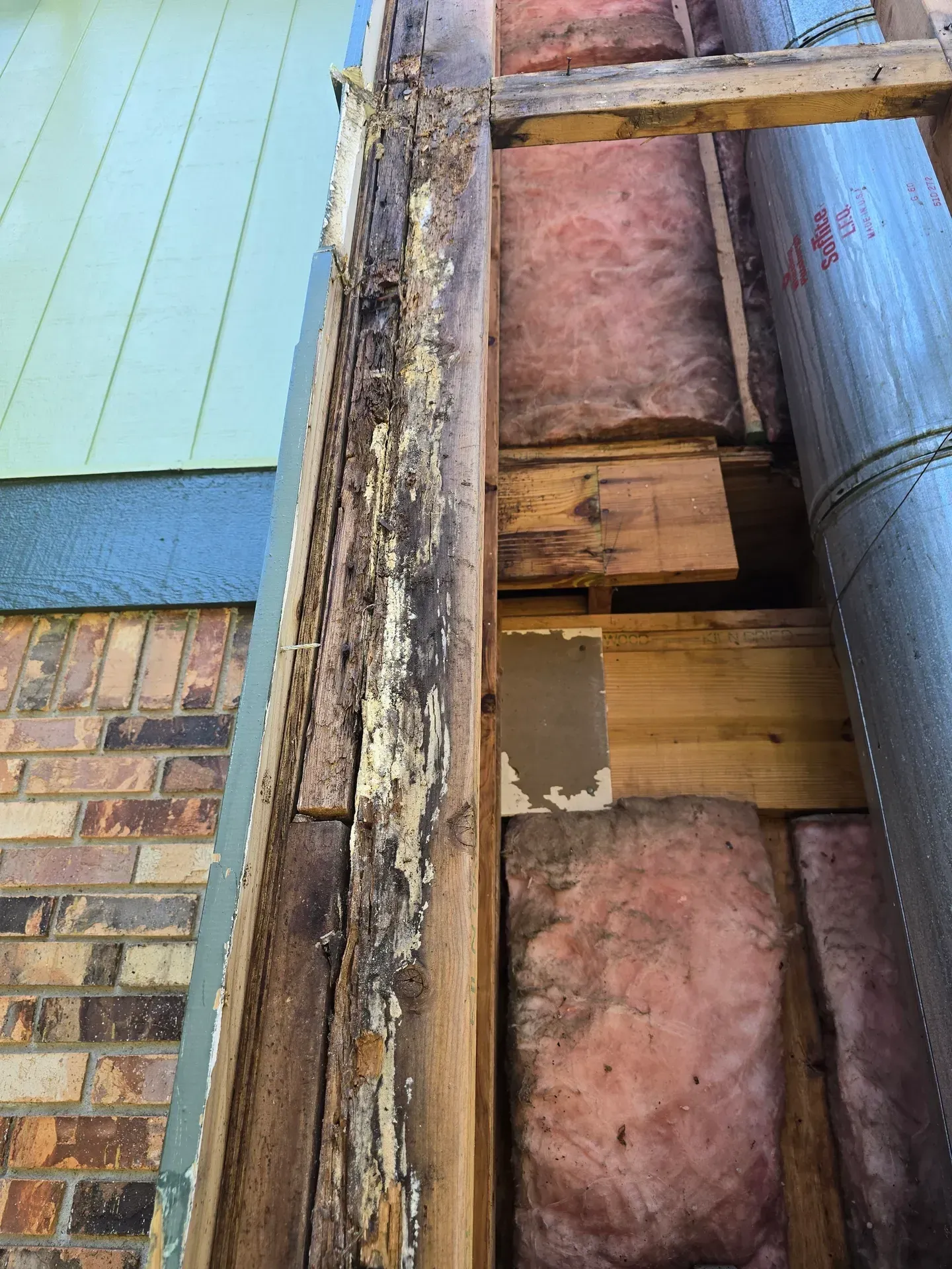 Damaged wood trim on a house exterior, exposing insulation and structural elements; weathered paint and rot visible.