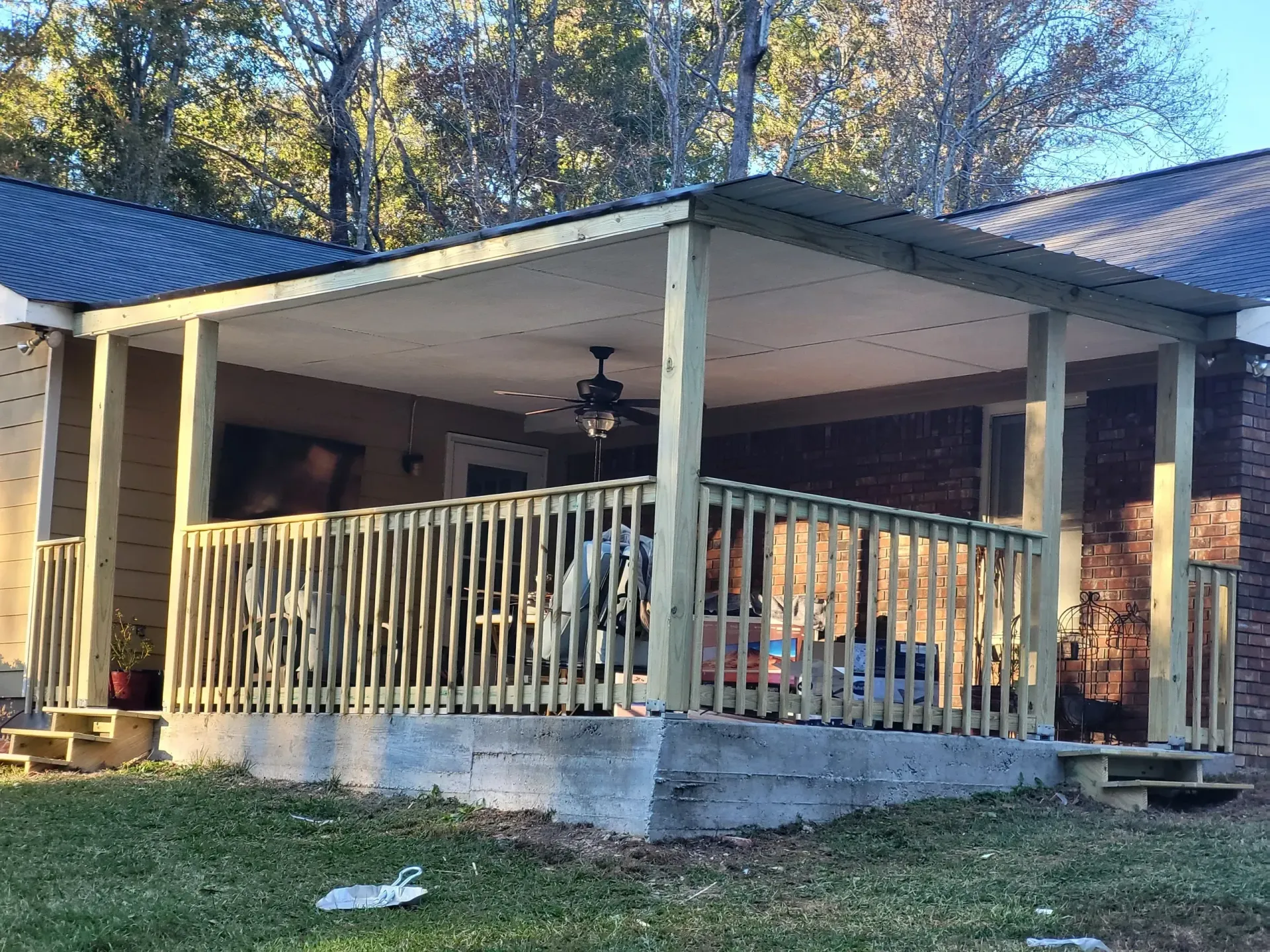 Covered porch with railing and concrete base, attached to a brick building.