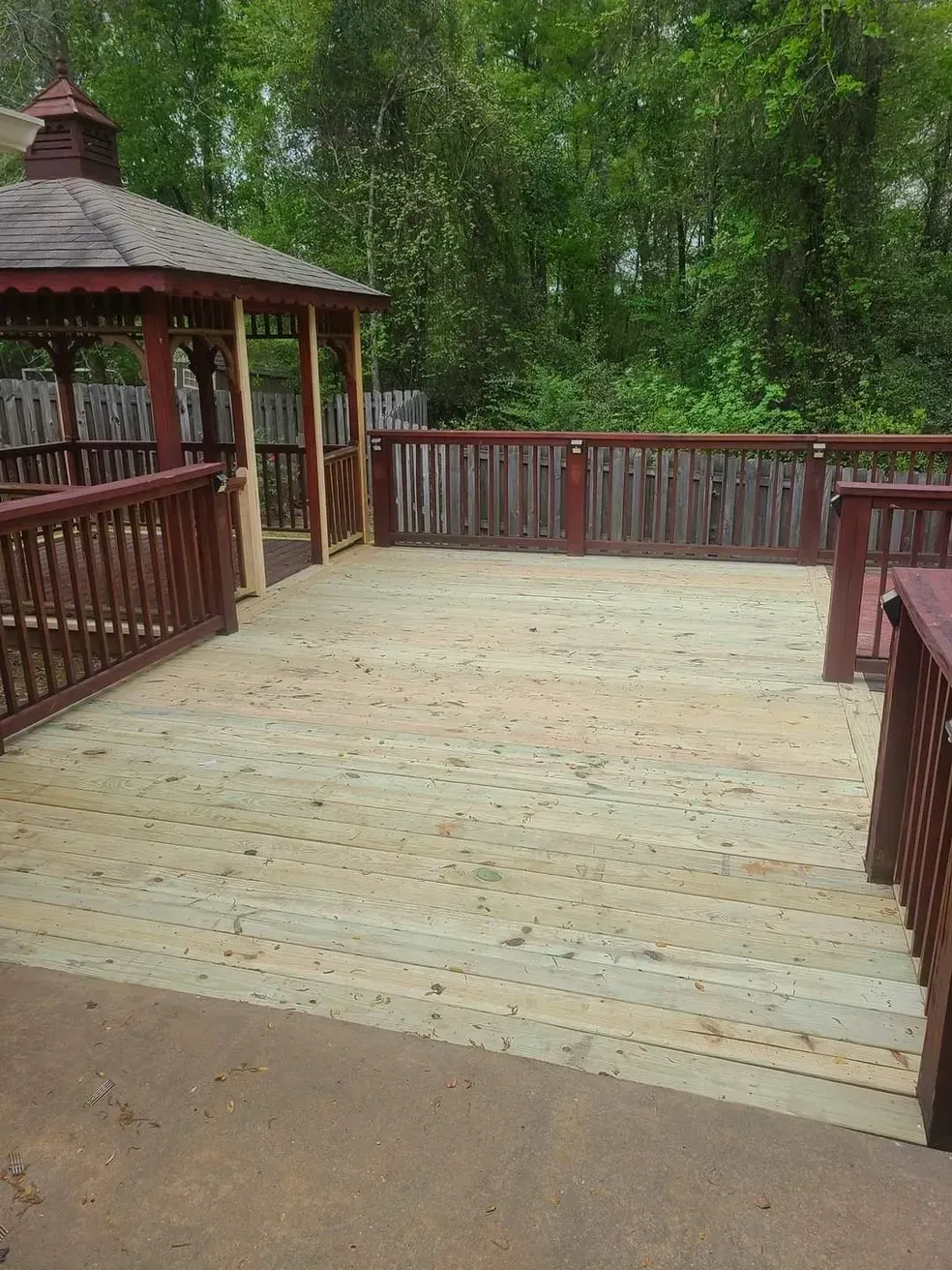 Wooden deck with a gazebo and railings, surrounded by trees.