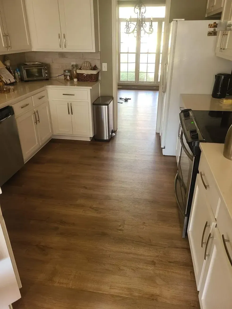 Kitchen with white cabinets, stainless steel appliances, and wood-look flooring. A door leads outside.