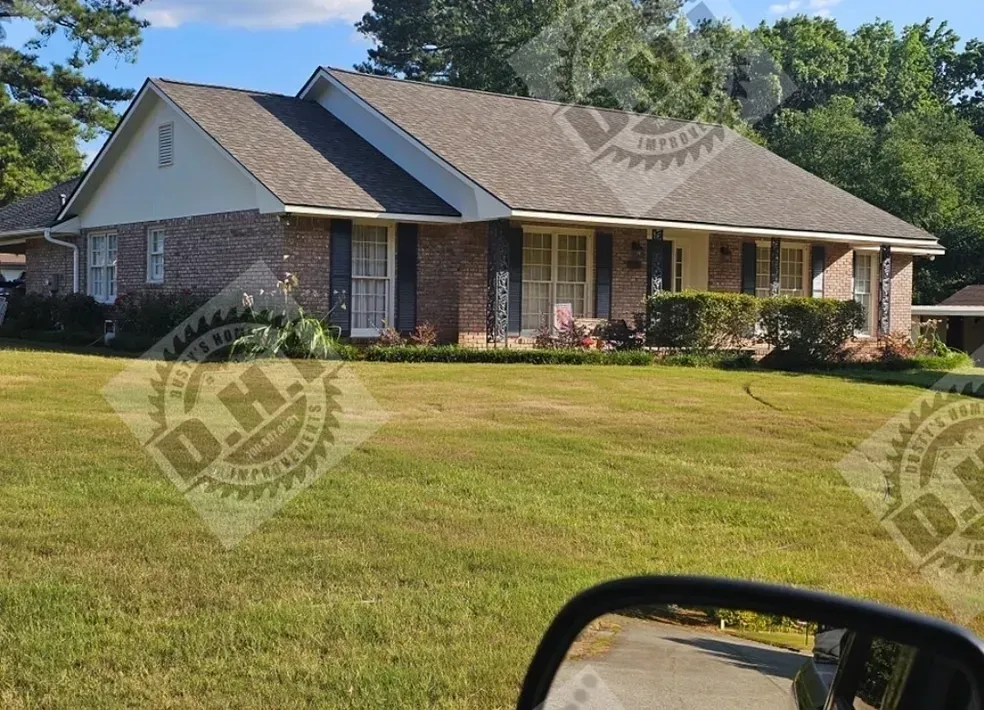 Brick ranch-style house with dark shutters and brown roof on a green lawn.