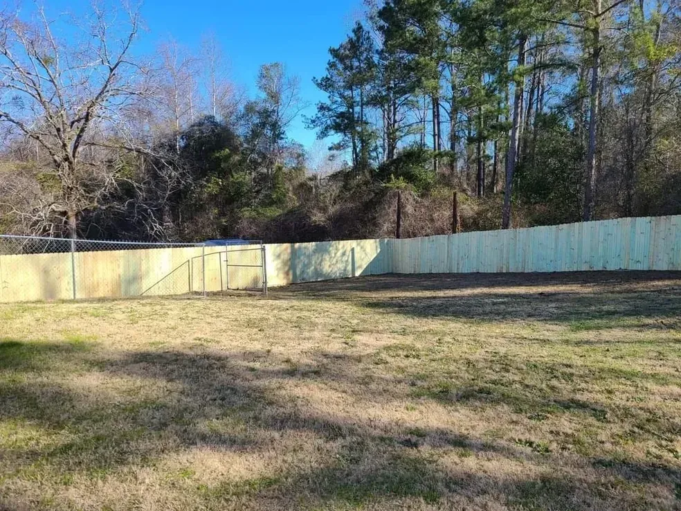 Wooden fence encloses a grassy backyard; trees in background under a clear sky.
