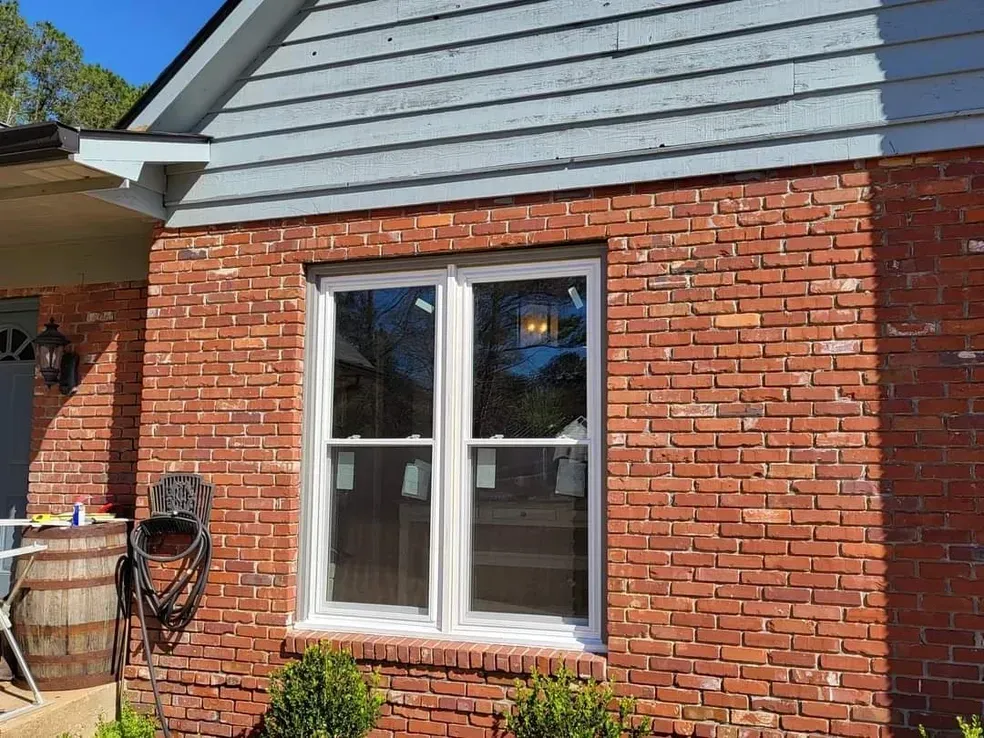Brick exterior wall with a new double-hung window. Blue siding above.
