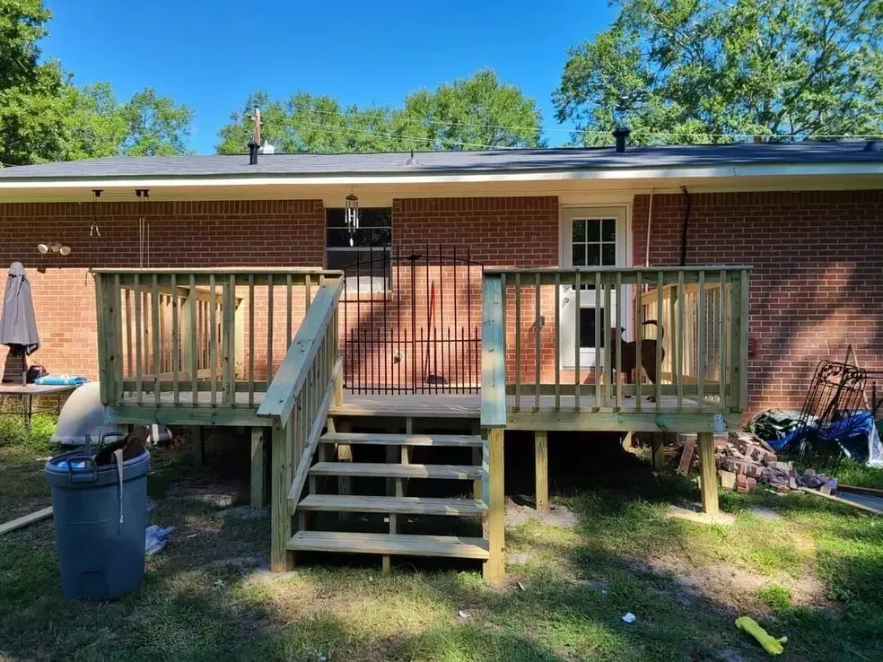 A new wooden deck with stairs attached to a brick house with a door, in a grassy backyard.