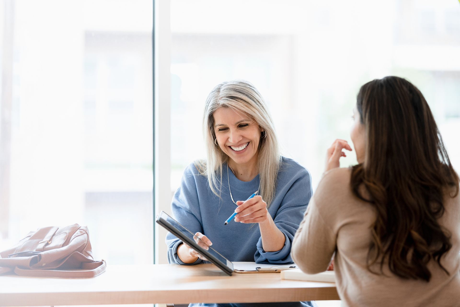 Two women are sitting at a table looking at a tablet.