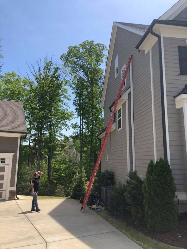 A man is standing in front of a house with a ladder attached to it.