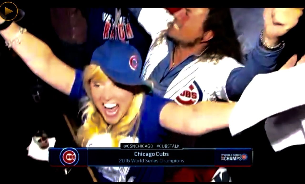 A woman wearing a chicago cubs hat holds her arms in the air