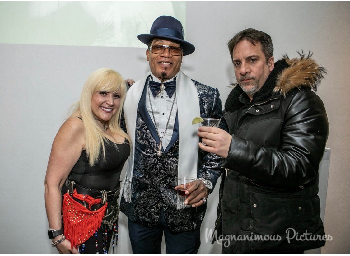 A man in a tuxedo is standing next to a woman and a man in a fur coat.