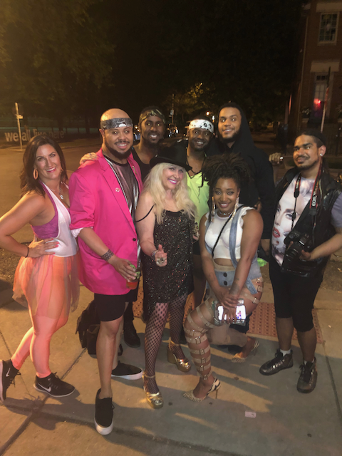 A group of people are posing for a picture on a sidewalk at night.