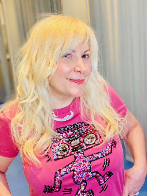 A woman with blonde hair is wearing a pink shirt with a monster on it.