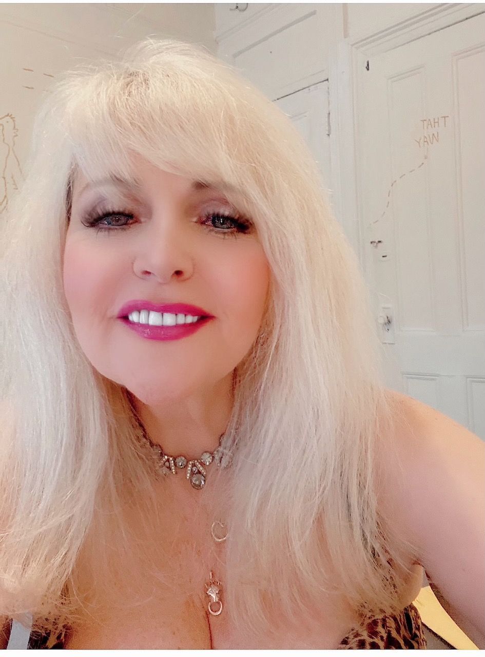 A woman with blonde hair is wearing a necklace and smiling