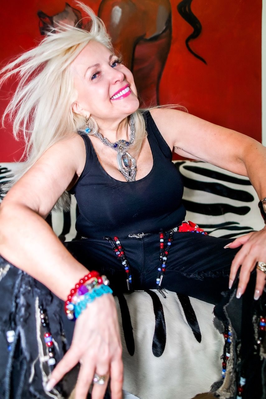 A woman in a black tank top is smiling while sitting on a bed