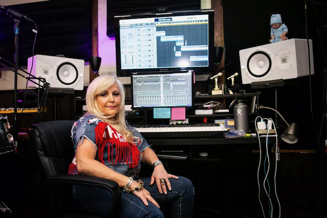 A woman is sitting in a chair in front of a keyboard in a recording studio.