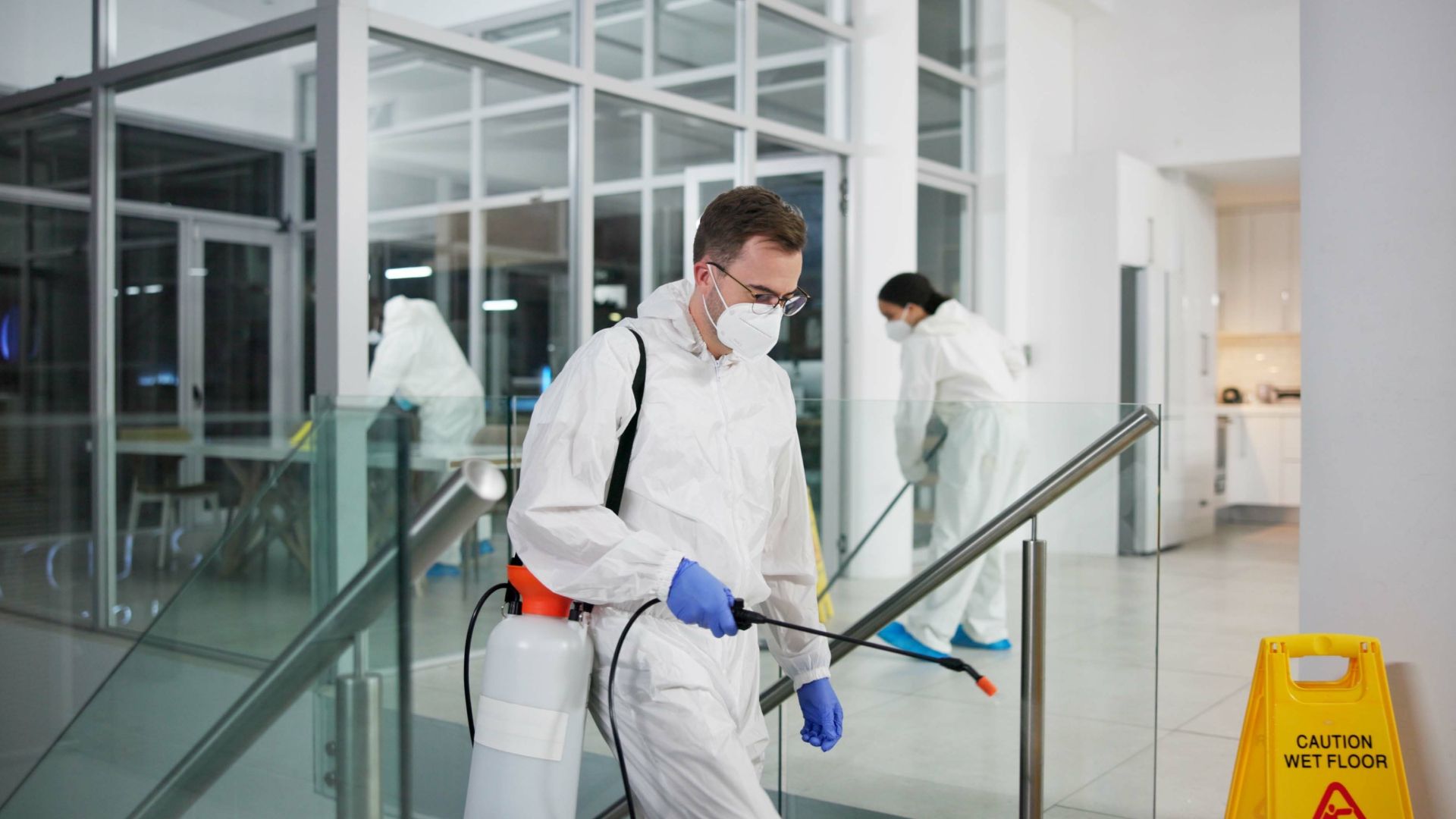 A man in a protective suit is spraying a floor in a building.