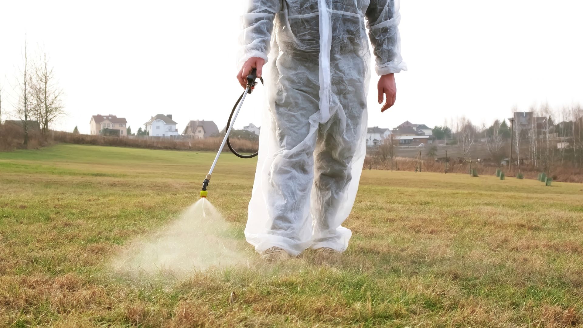 A man in a protective suit is spraying a field with a sprayer.