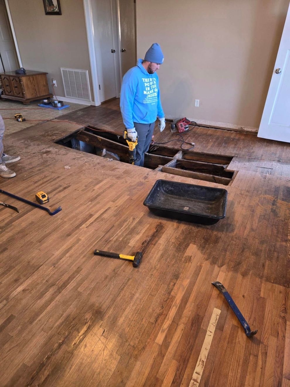 Person in blue hoodie standing in a partially removed floor during home renovation, with tools scattered around. Person in blue hoodie standing in a partially removed floor during home renovation, with tools scattered around.