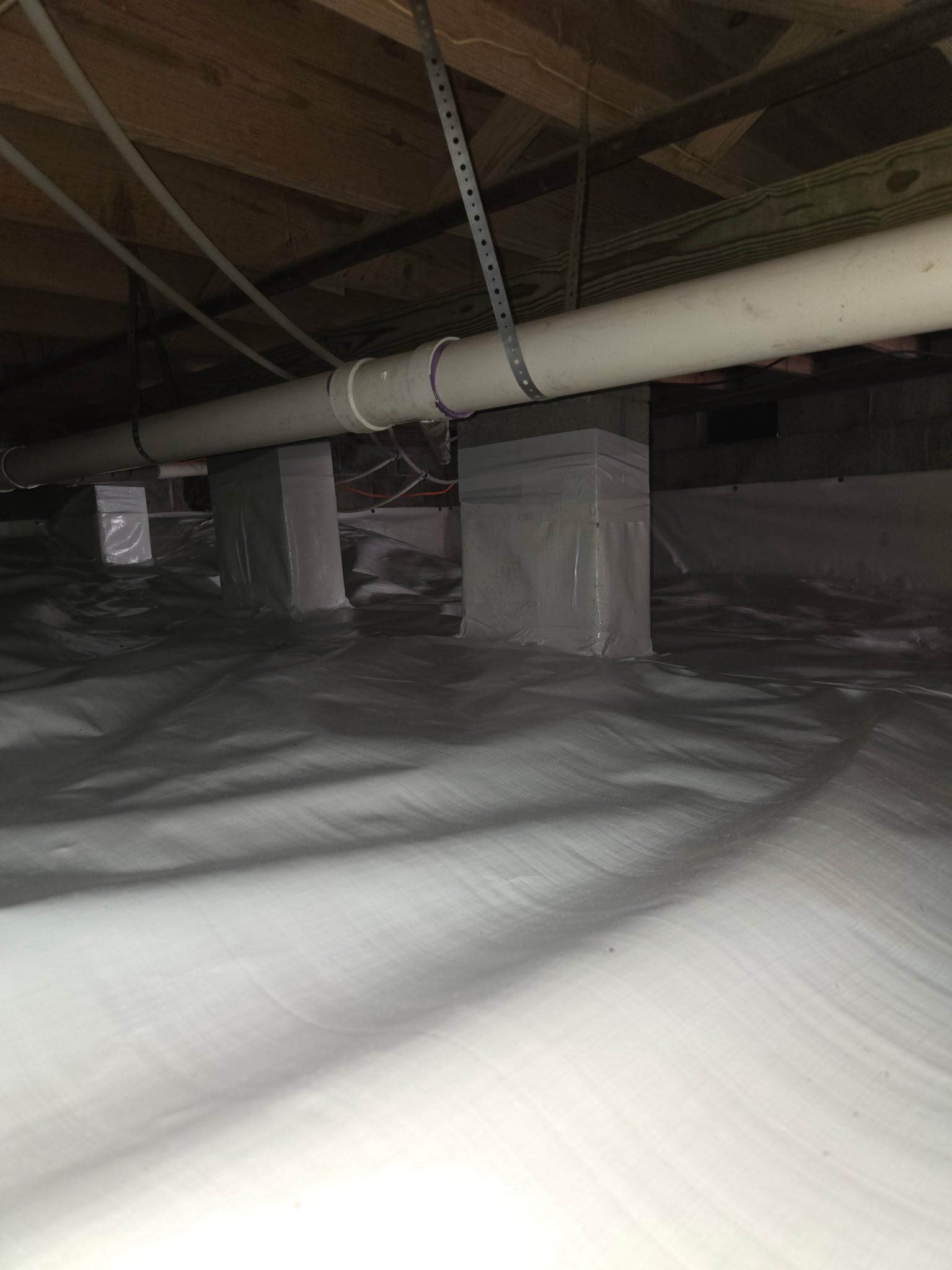 Crawlspace with plastic vapor barrier, exposed beams, and white insulation-covered ducts and supports Crawlspace with plastic vapor barrier, exposed beams, and white insulation-covered ducts and supports