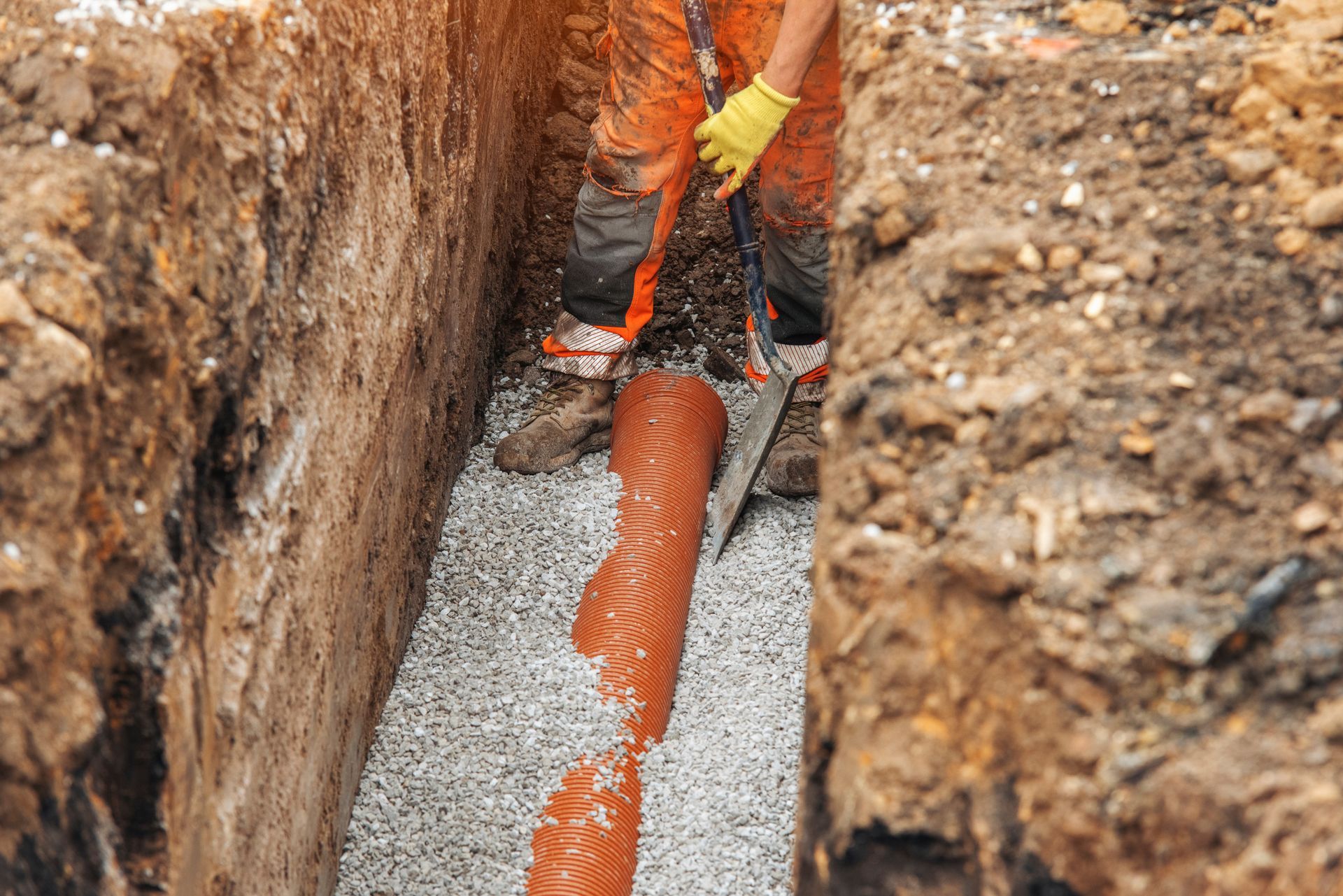 Worker laying orange pipe in a trench filled with gravel