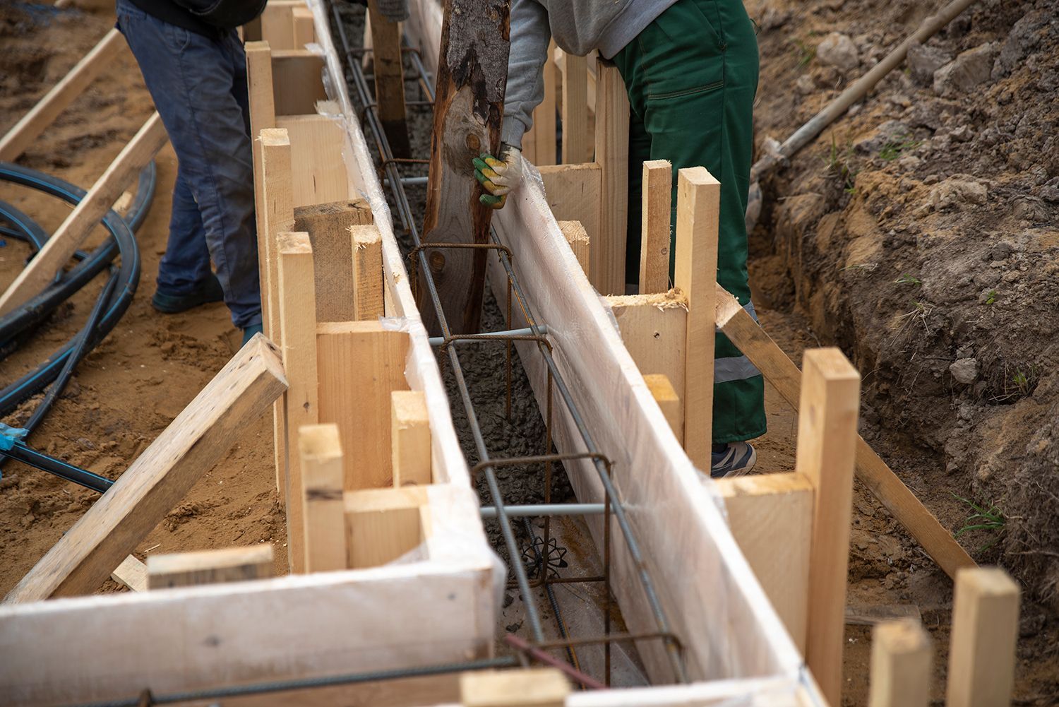 Workers installing rebar and wooden formwork for a concrete foundation trench Workers installing rebar and wooden formwork for a concrete foundation trench