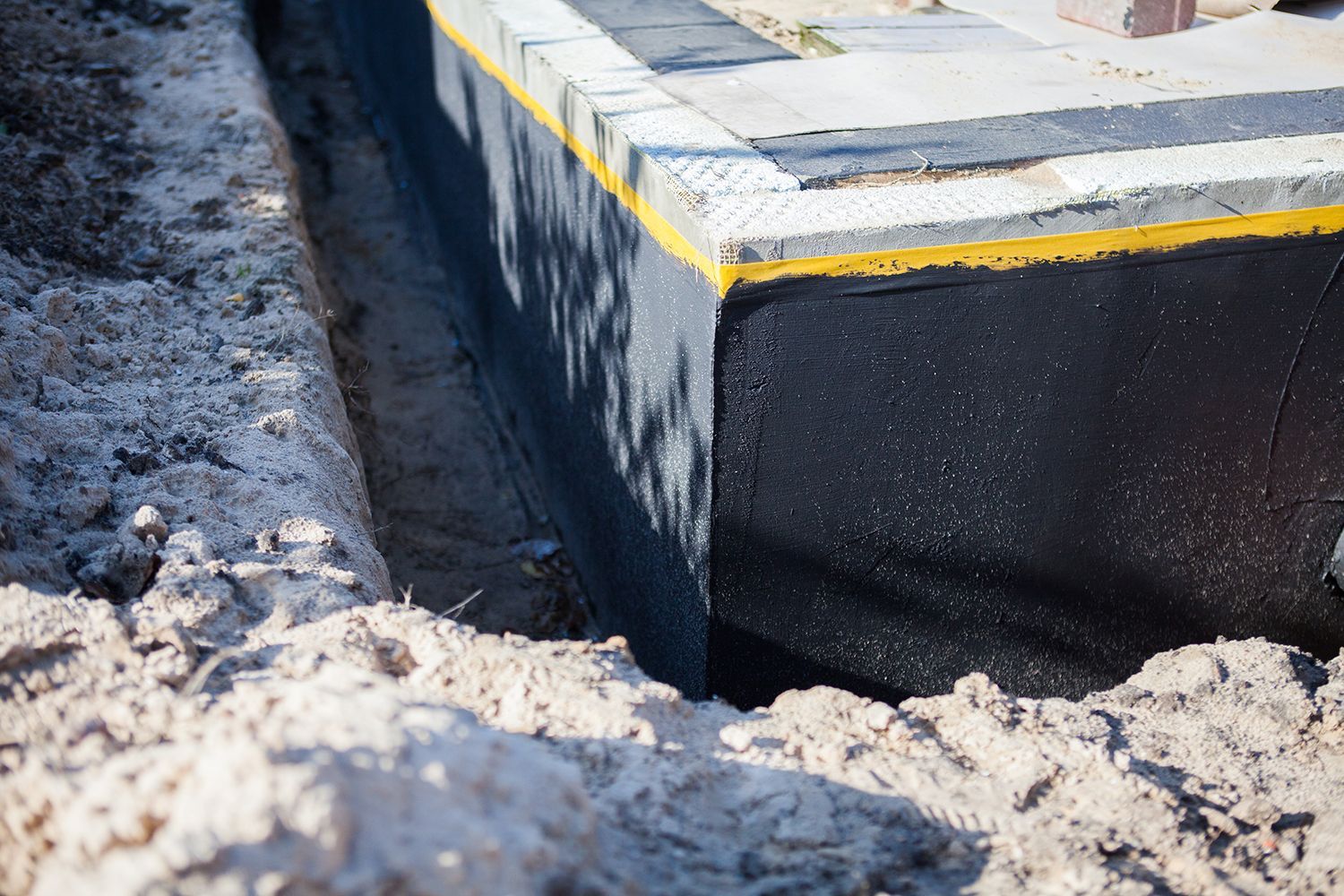 Close-up of a concrete curb or foundation edge with a yellow stripe, surrounded by dirt and snow. Close-up of a concrete curb or foundation edge with a yellow stripe, surrounded by dirt and snow.