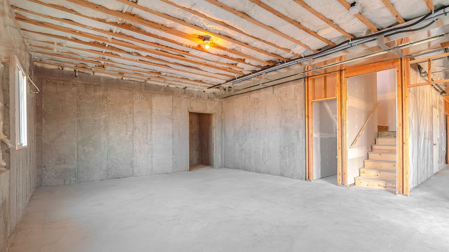 Empty unfinished room with bare concrete walls, exposed ceiling beams, and a doorway opening to a sunlit area. Empty unfinished room with bare concrete walls, exposed ceiling beams, and a doorway opening to a sunlit area.