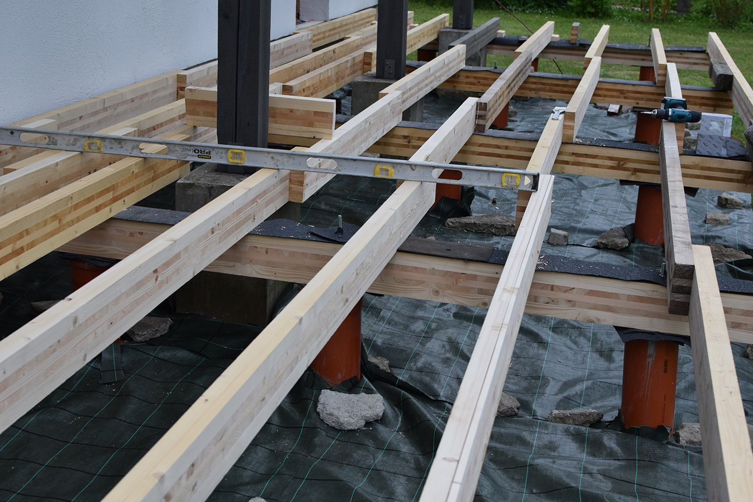 Wooden floor joists under construction on a raised deck with support posts and black sheeting below Wooden floor joists under construction on a raised deck with support posts and black sheeting below