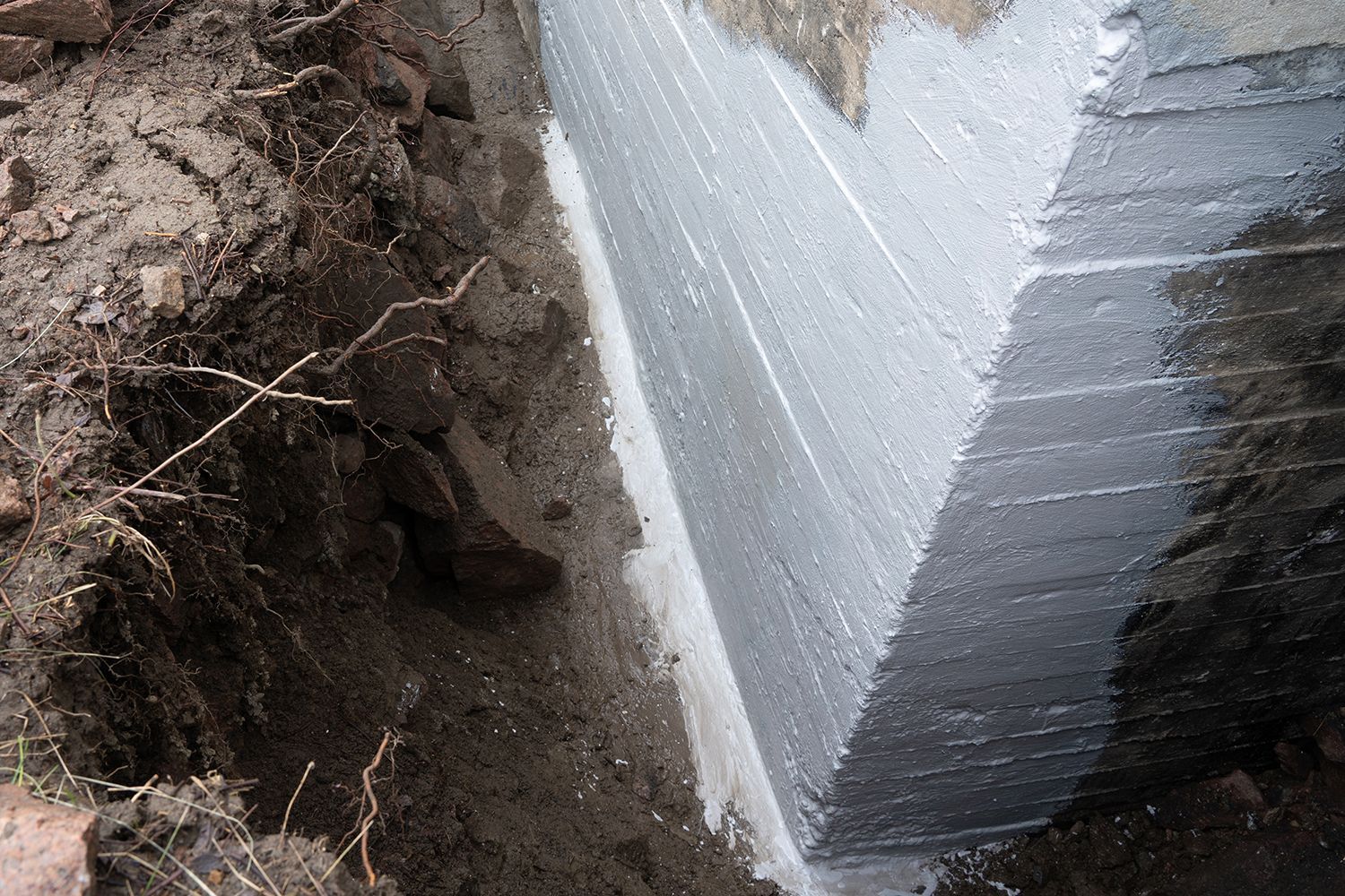 Excavated dirt beside a concrete foundation wall with white waterproofing coating Excavated dirt beside a concrete foundation wall with white waterproofing coating