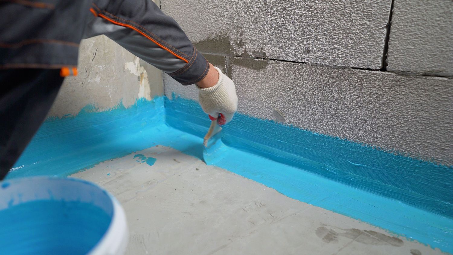 Person painting a blue waterproof seal along the edge of a rooftop with a brush Person painting a blue waterproof seal along the edge of a rooftop with a brush