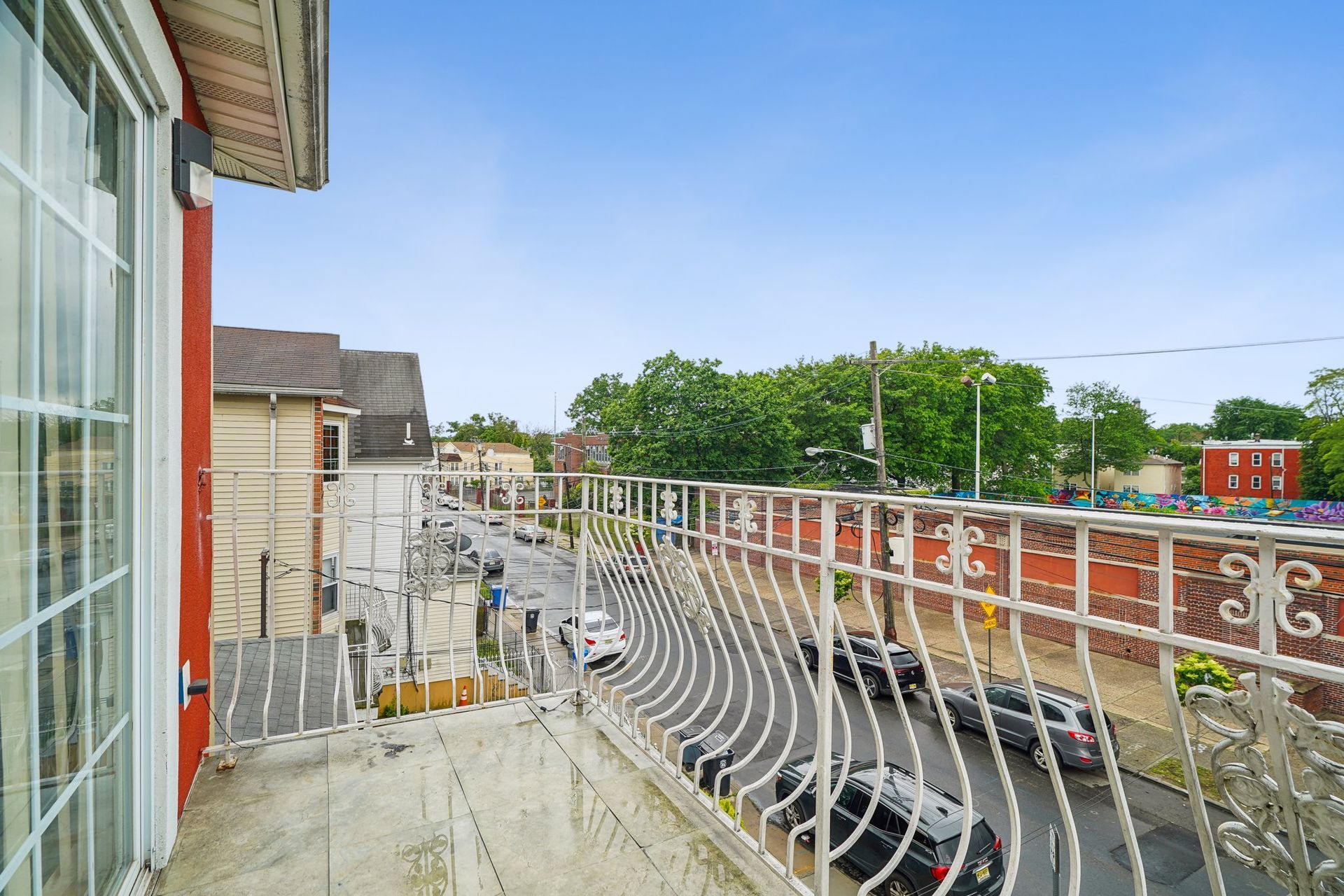 Balcony overlooking a street with parked cars, trees, and buildings on a bright day.