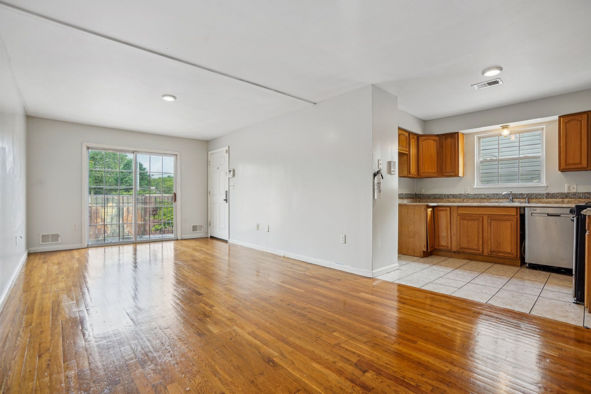 Bright, empty living space with wood floors, a half-wall to the kitchen, and sliding doors to the outdoors.