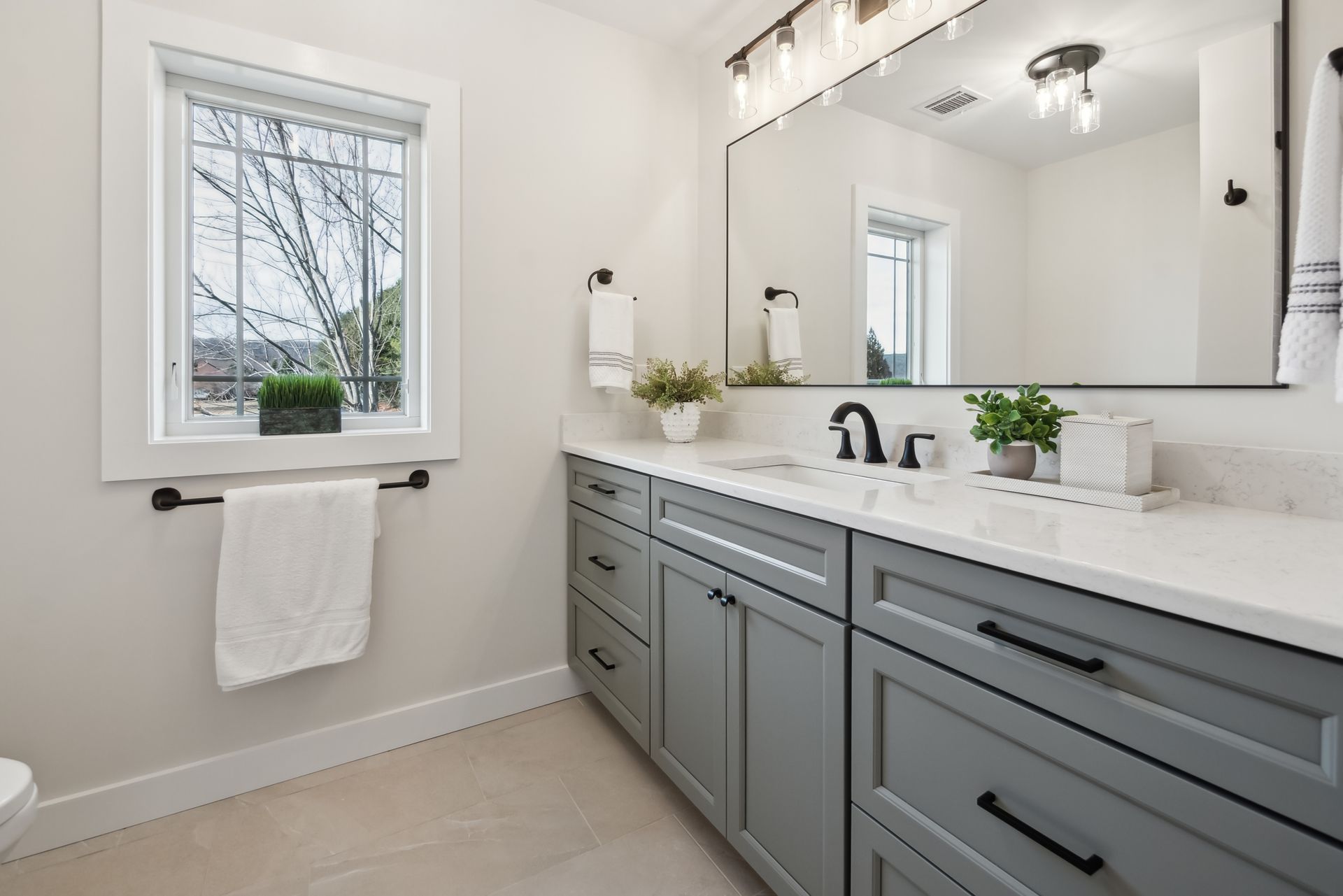 Bathroom with gray vanity, white countertop, large mirror, and window with a view.
